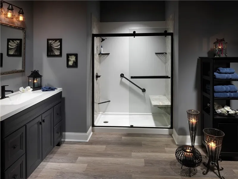 ADA-friendly walk-in shower with bronze grab bars, fold-down bench and frameless sliding glass door — aging-in-place remodel by Out This World Services