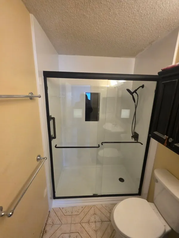 Modern black-framed sliding glass shower door over a smooth white solid-surface base — clean tub-to-shower conversion
