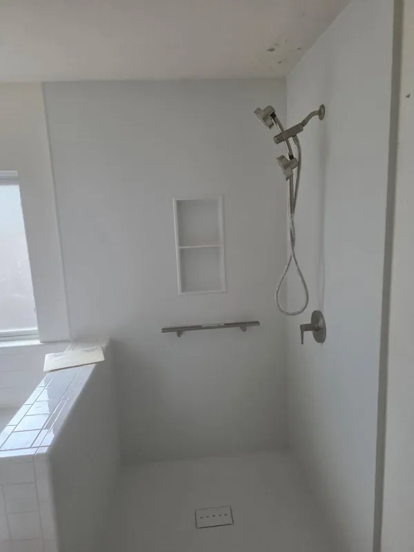 Clean all-white walk-in shower with recessed niche, ADA grab bar and dual handheld shower system installed in San Antonio