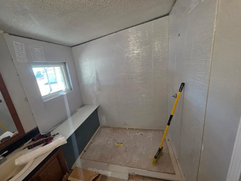 Mid-project: bathroom stripped down to the studs with new vapor-barrier wrap installed, ready for the solid-surface shower walls to go up